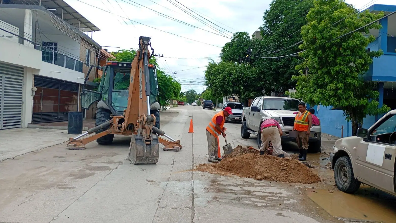 Cuadrilla con chalecos de seguridad excavando junto a una retroexcavadora en una calle
