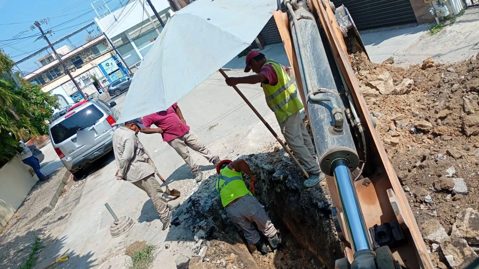 Trabajadores dentro de una zanja reparando una tubería, junto al brazo de la retroexcavadora